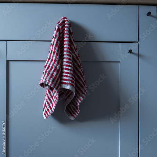 Kitchen cabinet door with a red and white striped towel hanging on the handle.