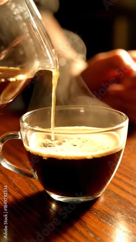 Freshly brewed coffee poured into clear glass cup on wooden table warm tones