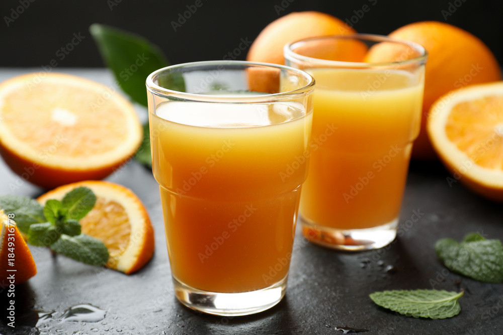 Fototapeta premium Fresh orange juice and fruits on black table, closeup
