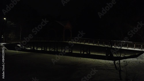 Night view of a snowy park bridge with street light. This footage is ideal for winter themes, park scenes, or nighttime city concepts.