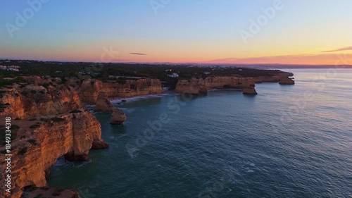 Marinha Beach, Cliffs, Sea Stacks and Atlantic Ocean at Sunrise. Green Scrubland. Aerial View. Algarve, Portugal. Moving Forward