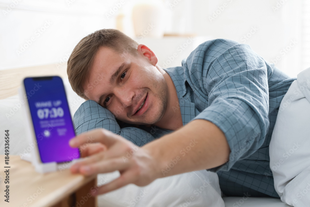 Fototapeta premium Man turning off alarm clock on smartphone in bed indoors