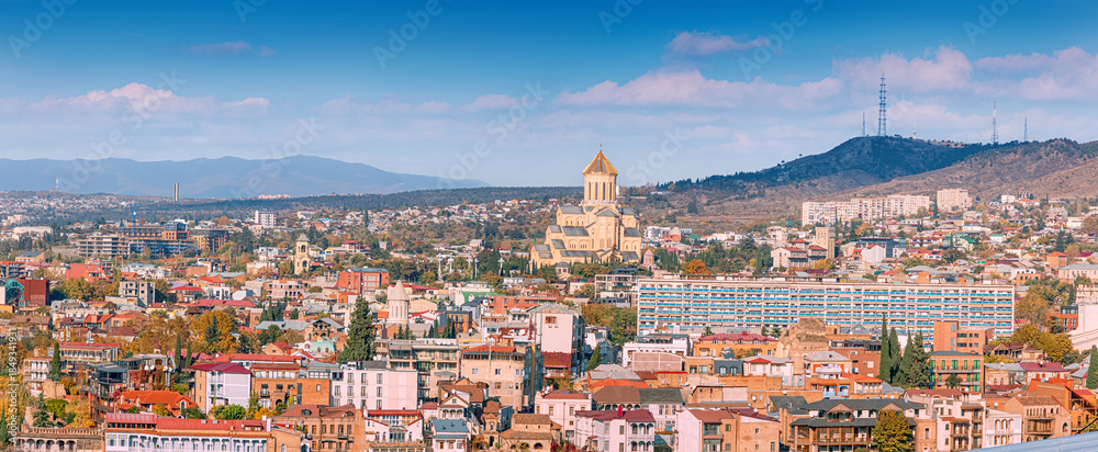 Panoramic view of Tbilisi cityscape featuring the Holy Trinity Cathedral and urban architecture against a clear blue sky