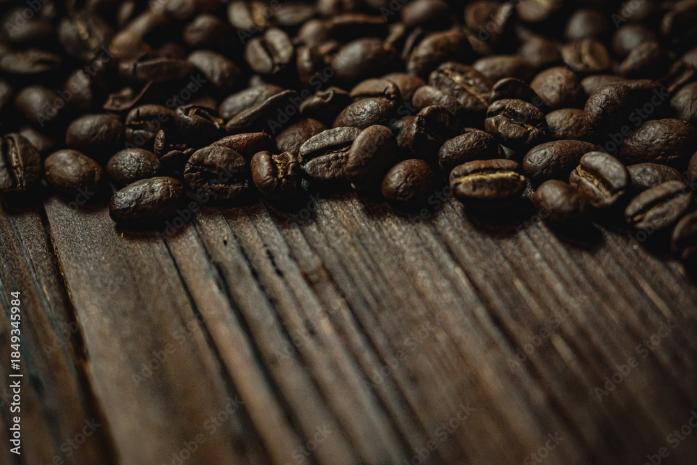 Fototapeta premium Roasted coffee beans scattered on a rustic dark wooden table, creating a rich brown texture and background for morning concepts