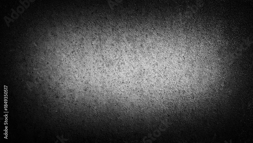Dark concrete texture background with soft vignette light in the center. Rough matte surface with subtle grain and gradient shadows. Minimal abstract backdrop suitable for banners, posters