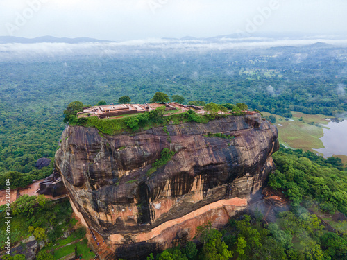 Aerial drone view of sigiriya rock fortress on a rainy day in Sri Lanka. Ancient UNESCO world Heritage site rising above lush green landscape under cloudy, overcast sky. Tropical nature and rain.