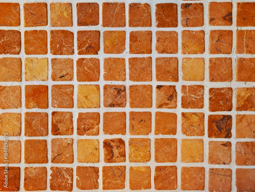 Natural stone mosaic tile texture. Square tesserae in earthy, orange and brown with veining and light-colored grout. Small marble slab cladding for interior wall, bathroom, kitchen, patio, pool.	
