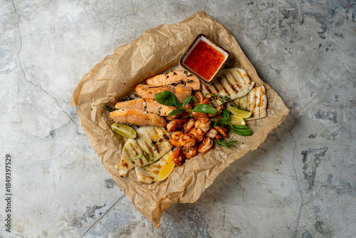 A vibrant seafood platter showcases beautifully grilled salmon and shrimp, garnished with fresh herbs and accompanied by zesty dipping sauce on a rustic surface. Perfect for sharing
