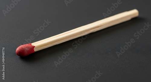 Wooden matchstick with red head laying on dark grey background surface