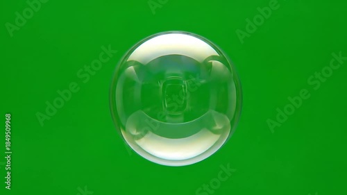 Clear soap bubble floating and popping against bright green screen background