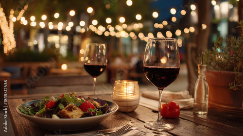 Romantic Dinner Setup with Wine Glasses and Salad on Outdoor Patio at Night with String Lights