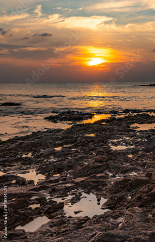 Dramatic sunset with sun reflection on a rocky beach in Khao Lak Thailand. Golden light illuminates the rocks, sea and sky, capturing a tranquil tropical coastal landscape at dusk.