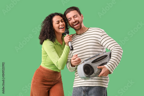 Fotografie Young couple with microphone and boombox singing on green background
