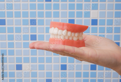 Hand holding dentures against blue bathroom tiles