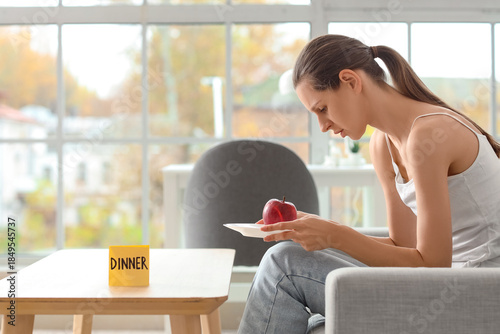 Tableau sur toile Young woman with apple for dinner sitting on sofa at home