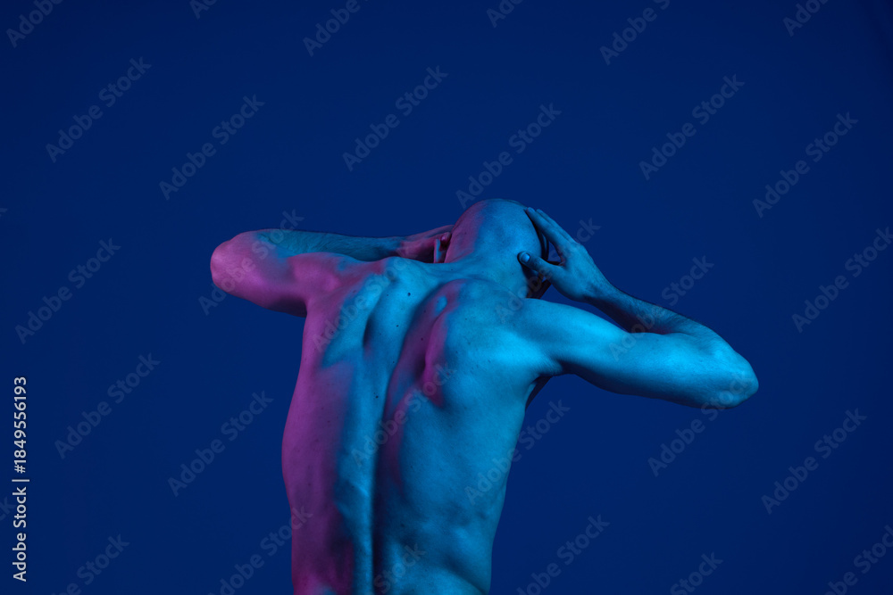 Obraz premium A man poses dramatically against a blue background, showcasing his muscular physique with vibrant lighting. The image emphasizes emotion and artistic expression, creating a striking visual impact.