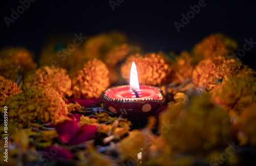 Closeup of Handmade Painted Diwali Clay Diya with Glowing Flames with Rose and Marigold Flowers Isolated on Black Background with Copy Space, Happy Deepavali or Diwali Festival Concept