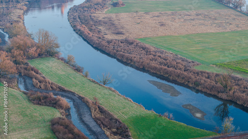 Ein Fluss schlängelt sich durch die Landschaft mit Wiesen und Bäumen, aufgenommen in der Dämmerung