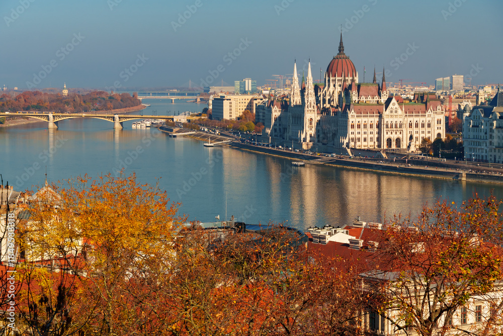 Fototapeta premium Budapest cityscape, panoramic view of city and Danube River, Parliament building with Margit bridge and beautiful architecture in autumn season, trees, branches and yellow leaves in foreground