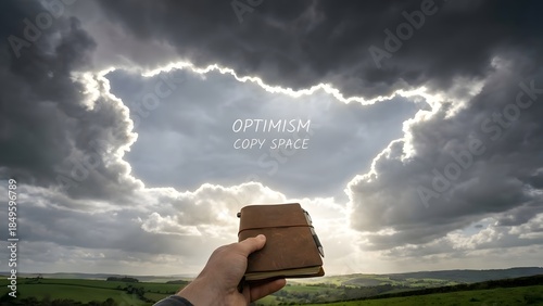 Hand Holding Bible Under Dramatic Stormy Sky.