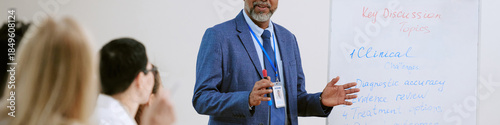 Photography Senior Black man presenting to diverse group, standing near whiteboard with medi