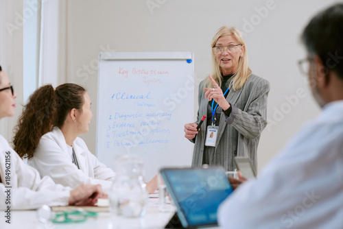 Φωτογραφία Middle aged Caucasian woman leading medical meeting, gesturing while standing ne