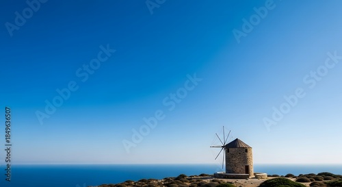 Traditional stone windmill overlooking the Aegean Sea on the island of Karpathos, Greece, under a clear blue sky.