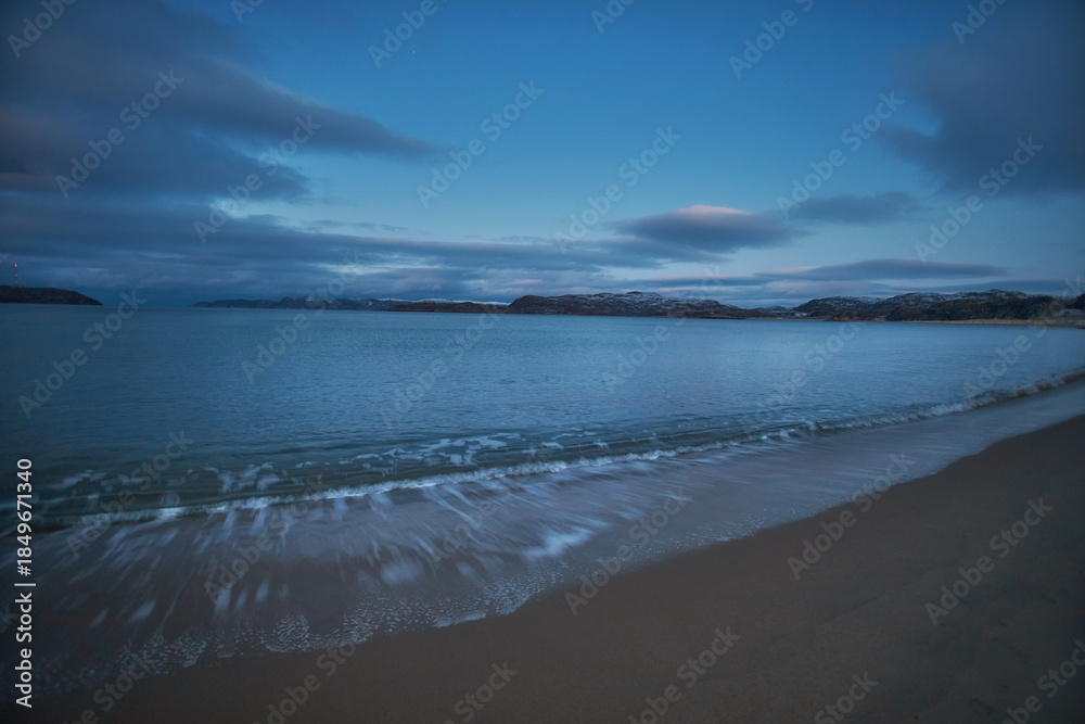 Fototapeta premium View of the coast in Teriberka, Russia, during twilight with calm water and distant hills visible on the horizon