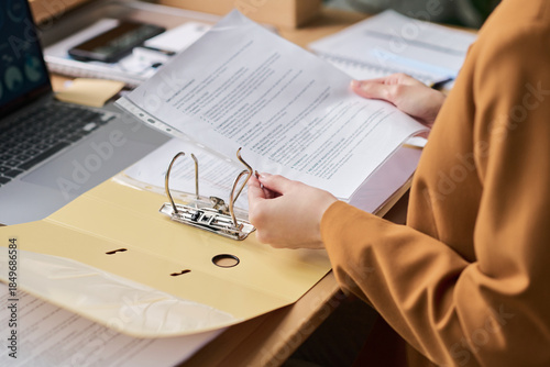 Photos Young adult woman organizing documents in office setting, holding printed papers