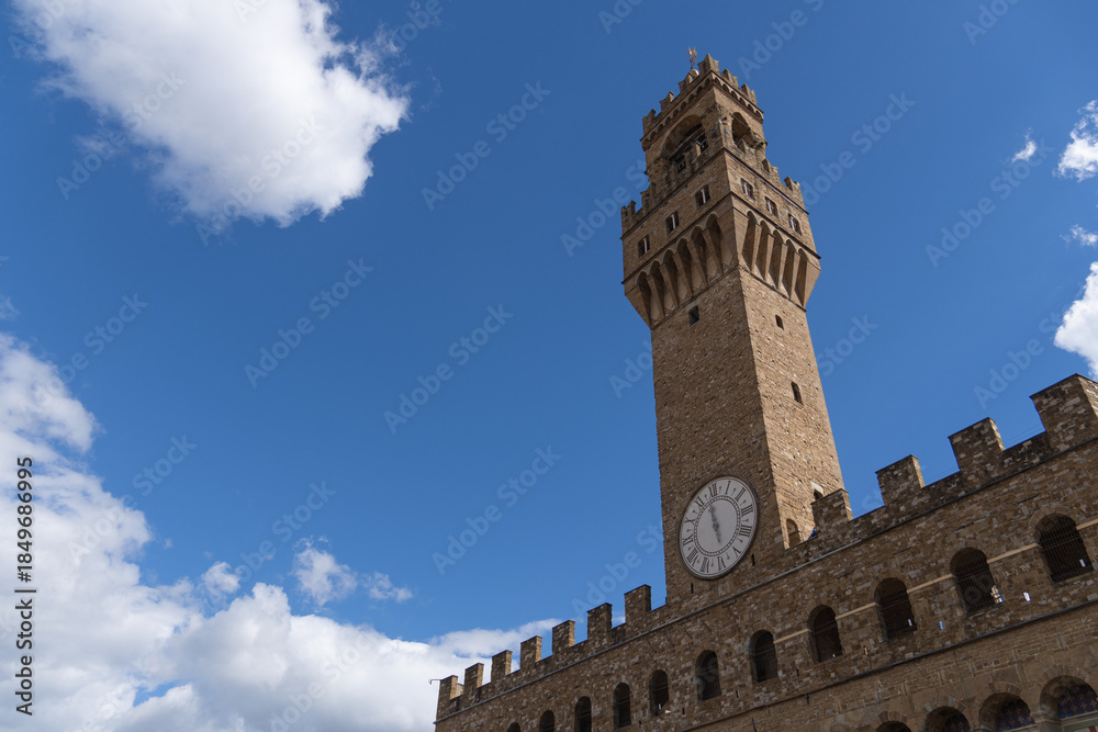 Fototapeta premium Palazzo Vecchio clock tower in Florence under blue sky. View of the iconic Palazzo Vecchio clock tower in Florence, Italy. Historic architecture and medieval landmark in the city center with a bright 