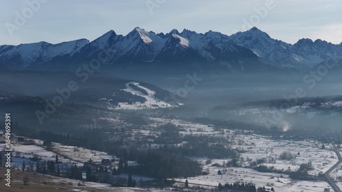 Aerial drone view of the Tatra Mountains from Czarna Gora near Zakopane, showing winter mountain range, forested hills, village landscape and alpine scenery during calm evening light