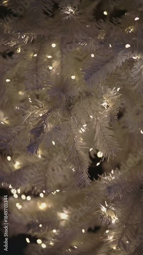 A close-up view of a white Christmas tree adorned with warm white lights. The branches are fluffy and create a cozy holiday atmosphere.