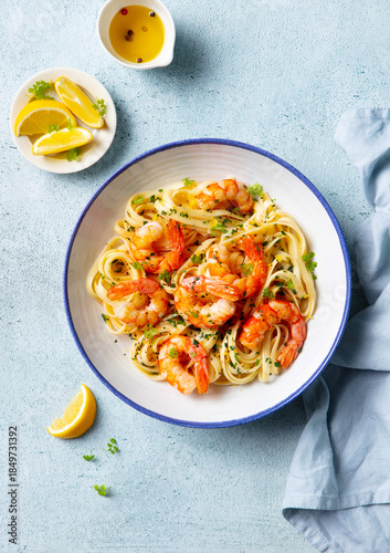 Delicious shrimp pasta dish with lemon accents and fresh herbs. Light blue background. Top view.