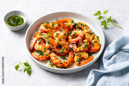 Grilled shrimps with chimichurri sauce on a white plate. Light grey background. Close up.