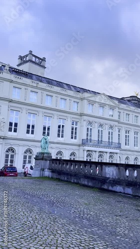 Palace of Charles de Lorraine, Brussels, Belgium. A cobblestone street runs through a historic area with large buildings on either side. The sky is cloudy with a hint of blue.