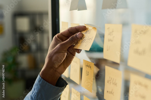 Photos Black man organizing sticky notes on glass wall, hand placing note labeled new s