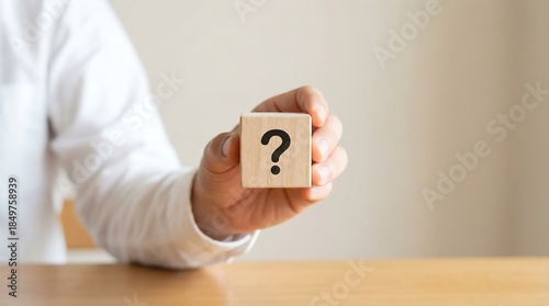 A person holds a wooden block with a question mark, conveying curiosity and inquiry. This image can be used to represent puzzlement