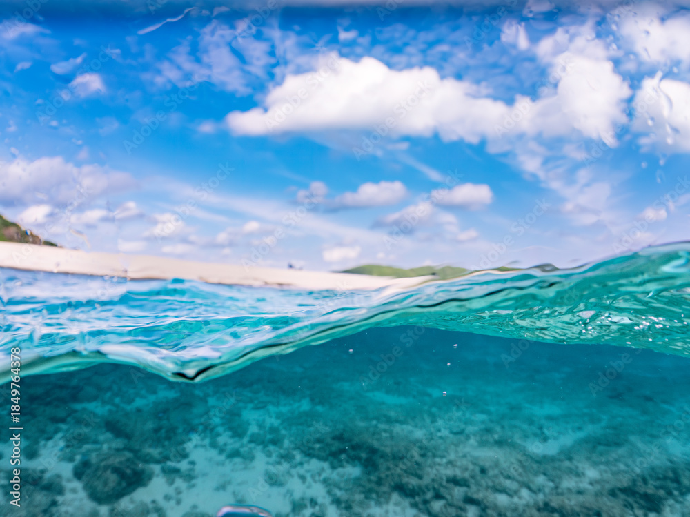 Fototapeta premium 嘉比島の美しい白砂ビーチの半水面撮影。 美しいサンゴ礁と熱帯魚の群れ。 嘉比島沖縄県 島尻郡慶良間諸島座間味島-2025 沖縄本島から40km西方の諸島。30以上の島嶼群全体が国立公園に指定。珊瑚礁の青い海と白い砂浜は世界屈指の美。貴重な動植物が多数生息。 