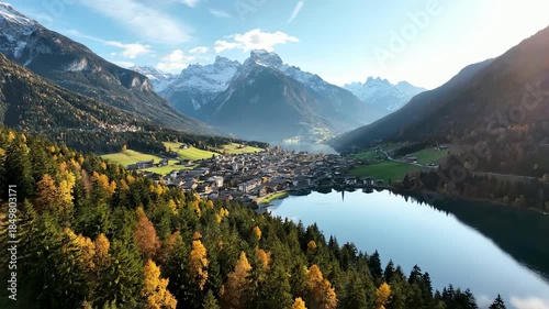 Aerial drone view of a charming alpine village nestled beside a serene lake surrounded by colorful autumn foliage and majestic mountains