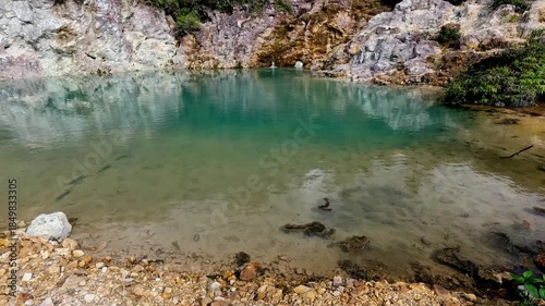 Tilt up to reveal the pool of blue clear water and rugged white lime and red wall of rocks in the JABA sulfur lagoon. Tanjay, Negros Oriental, Philippines