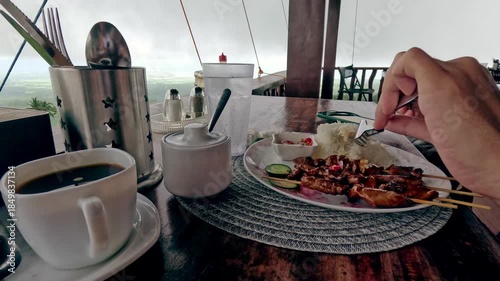 Candid peaceful scene eating pork barbecue skewers served with rice while enjoying the view of the foggy mountain landscape