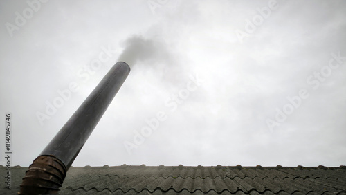 old metal chimney on the roof with grey smoke coming out