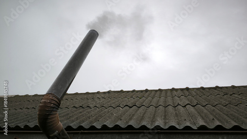 old metal chimney on the roof with grey smoke coming out