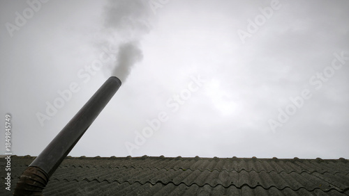old metal chimney on the roof with grey smoke coming out