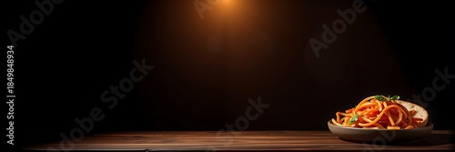Artistic food photography of spaghetti pasta with basil and bread on a rustic wooden table, illuminated by a warm spotlight against a dark background.