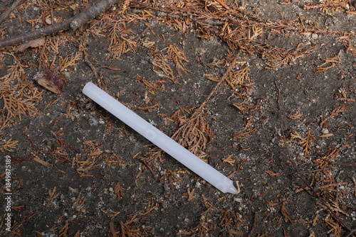 Fotografie A white candle is laying on the ground in a field of dried leaves