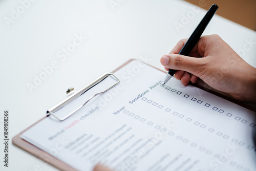 Photos Person filling mental health checklist on clipboard with pen, psychological assessment, self evaluation, healthcare screening and wellbeing awareness concept