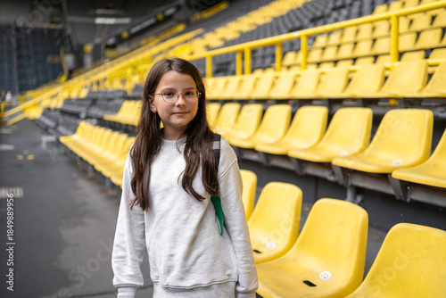 Smiling teenage girl on empty football stadium during excursion, travel education and fun concept