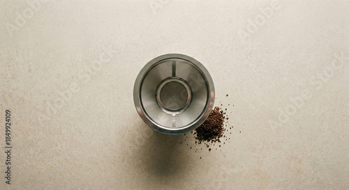 Stainless steel reusable coffee filter placed on a neutral matte surface, sustainable lifestyle concept.