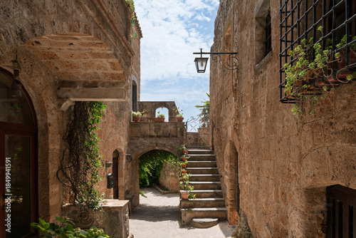 Italy - Bagnoregio - Civita di Bagnoregio - Shaded courtyard passage with exterior stair, arched tunnel and lantern between warm tuff walls